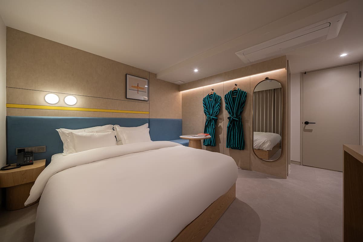 A modern hotel room with a large bed, bedside table, robe hooks, and a mirror.
