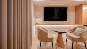 A modern living room with two upholstered chairs, a round coffee table, a flat-screen TV mounted on the wall, and a floor lamp. - Villa de Boni (Seoul)