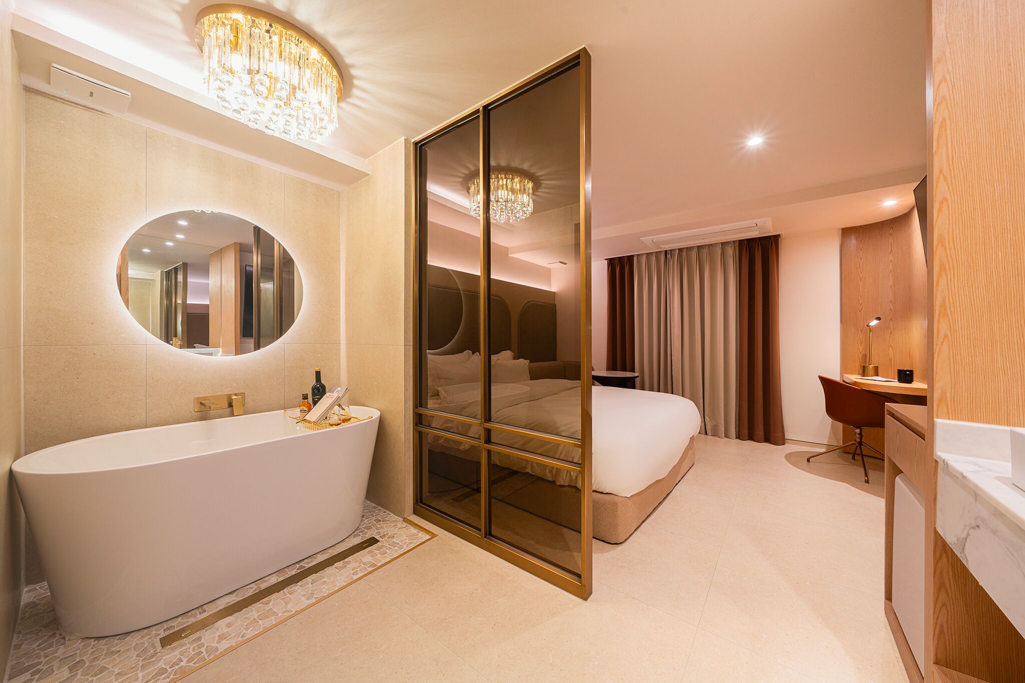 A modern hotel room with a large bathtub, a mirrored wardrobe, a bed, a desk, and a separate bathroom area.