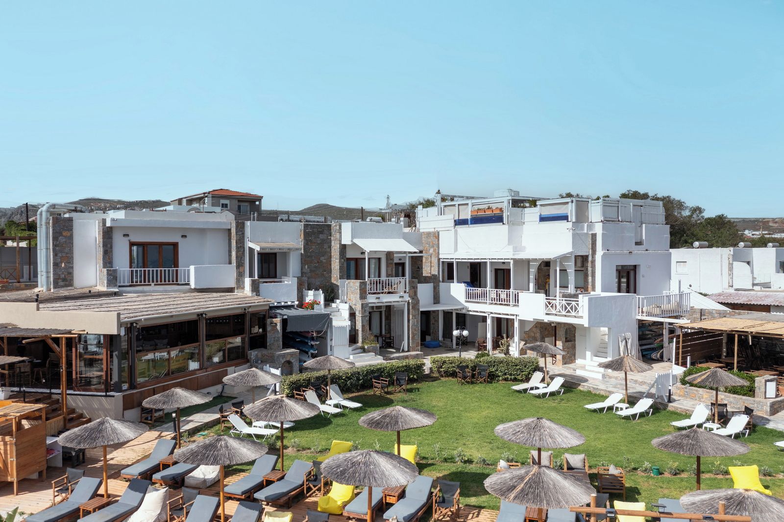 A resort with multiple white buildings, outdoor seating areas with umbrellas, and a well-maintained lawn.