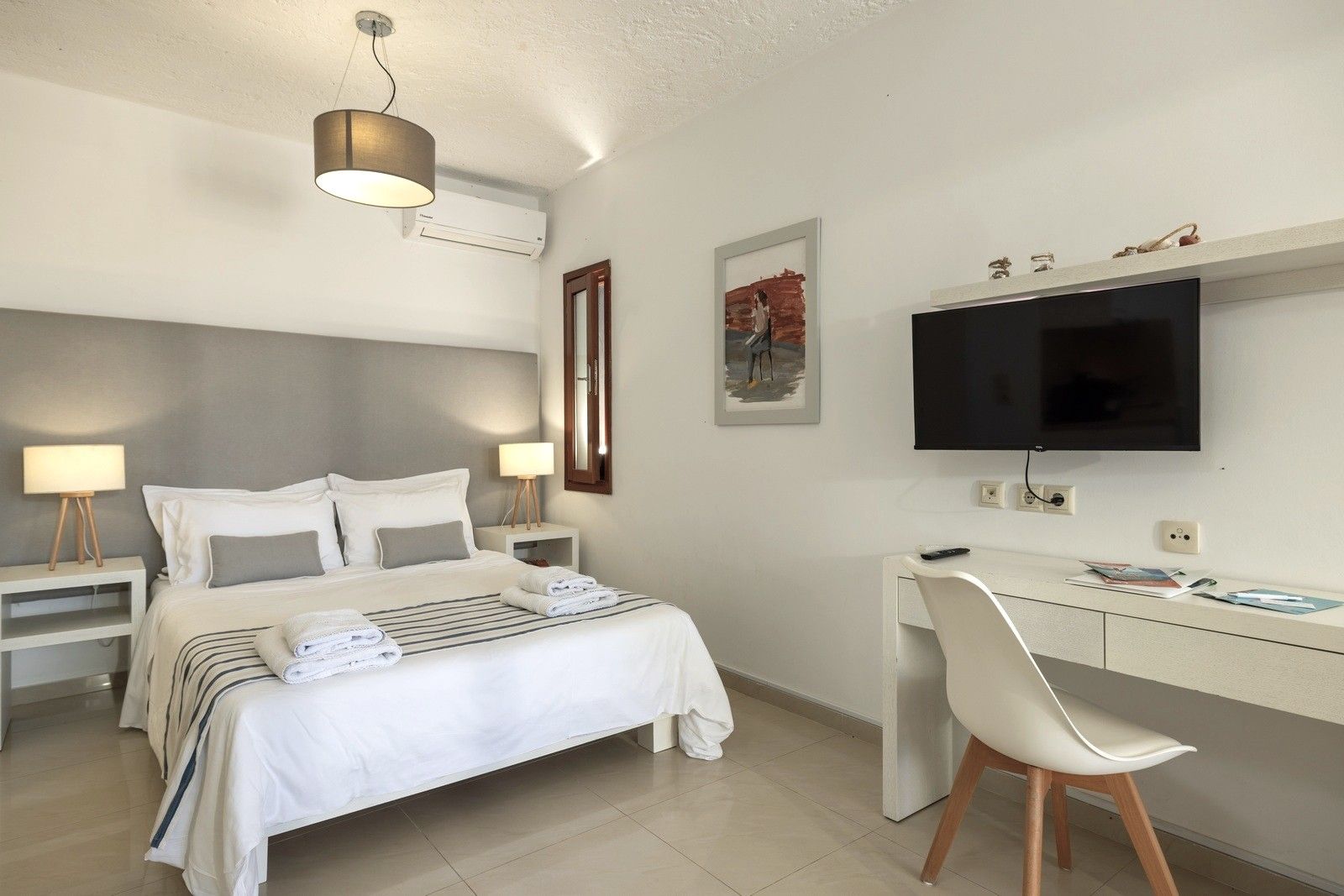 A hotel room with a bed, bedside lamps, a desk with a chair, a flat-screen TV, and artwork on the wall.