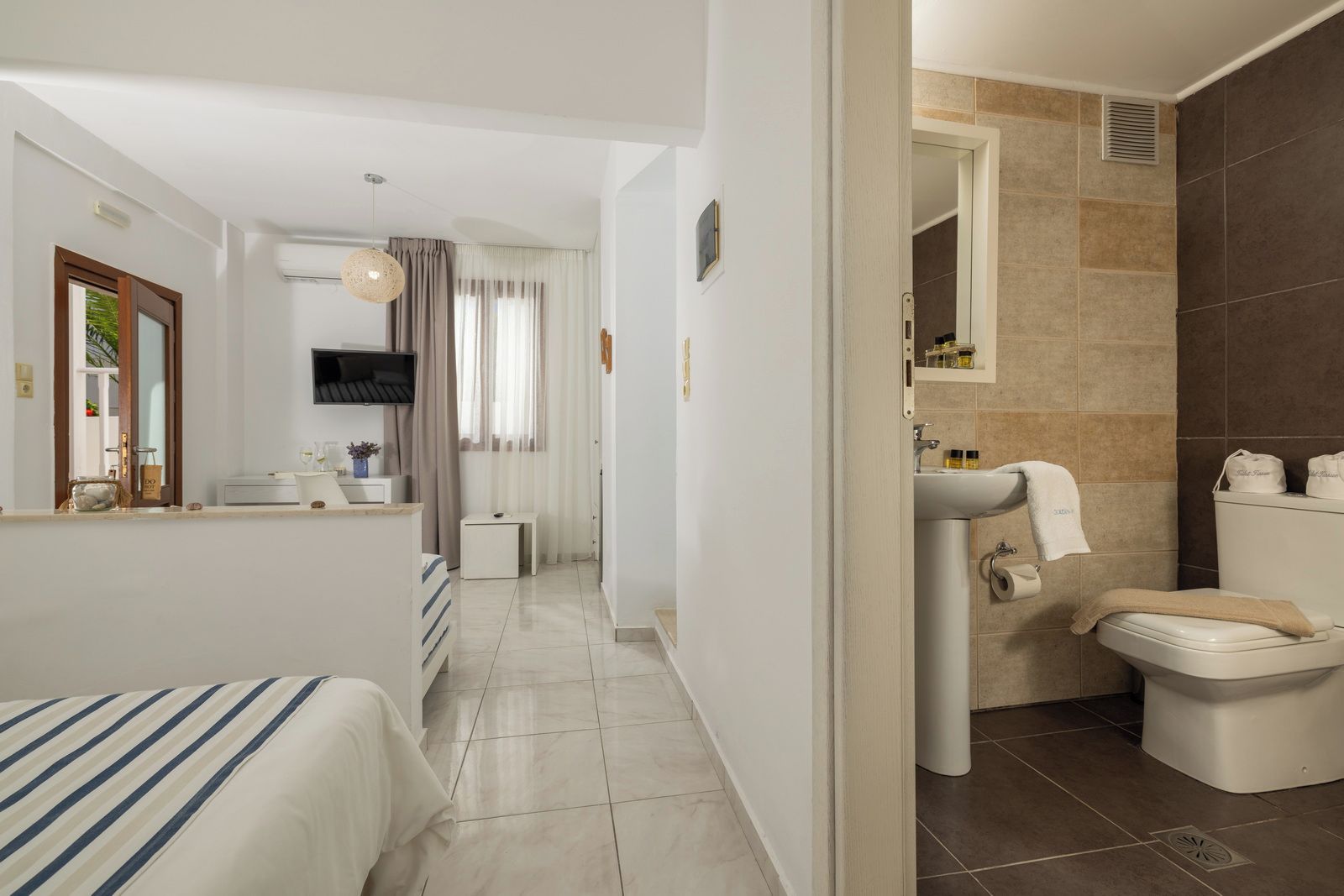 Een hotelkamer met een bed, een klein nachtkastje, een aan de muur bevestigde televisie, een badkamer met toilet, wastafel en douche.