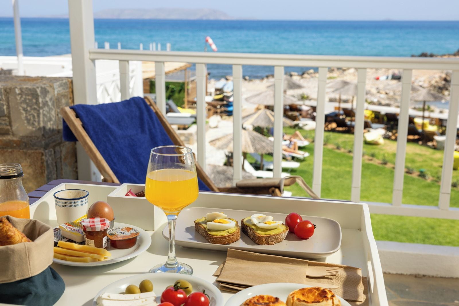 A table with breakfast items, a glass of orange juice, and a view of the beach and umbrellas.