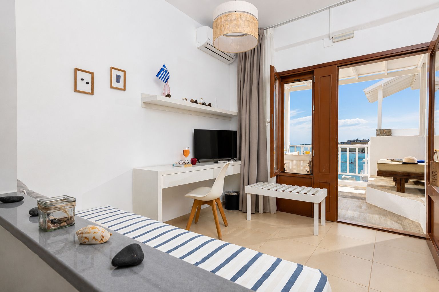 A modern room with a desk, chair, and a view of the sea through a glass door.