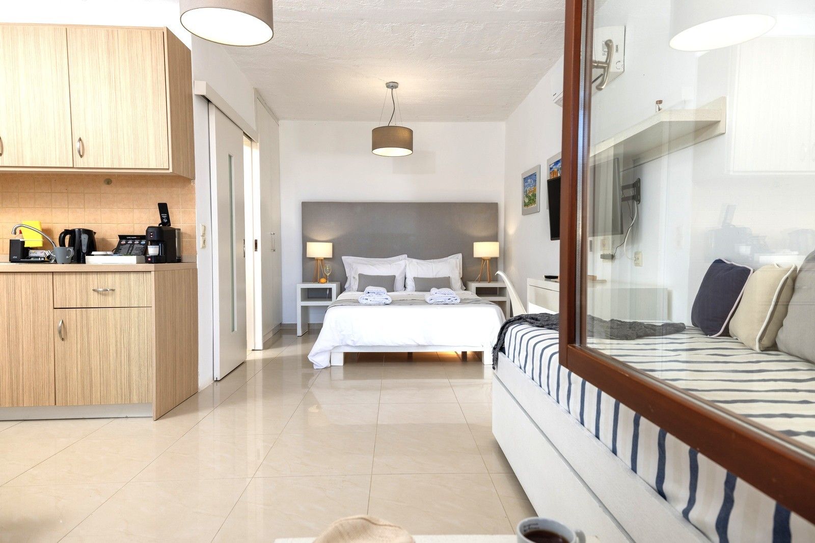 A modern hotel room with a bed, bedside tables, a desk, and a kitchenette.