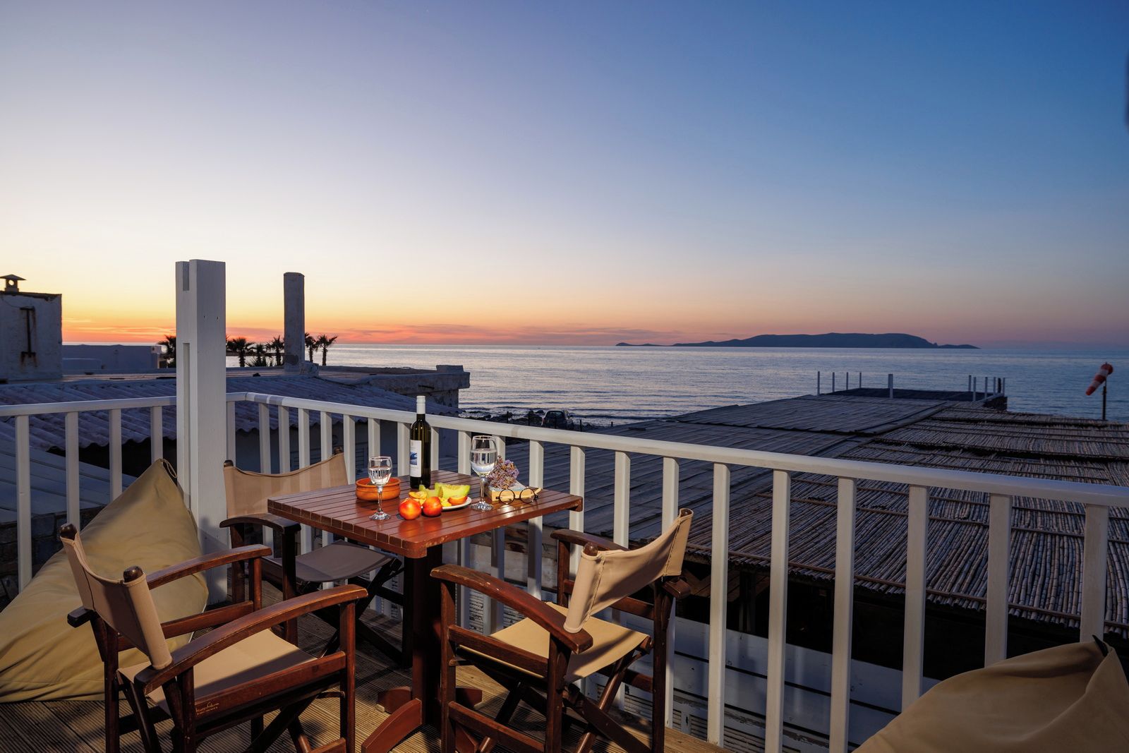 Een terras met een gedekte tafel voor twee, met uitzicht op de kust bij zonsondergang.