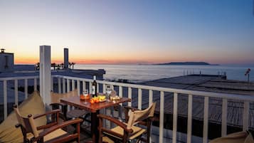 Een terras met een gedekte tafel voor twee, met uitzicht op de kust bij zonsondergang.