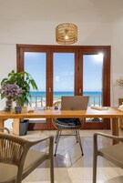 Un comedor con vista al mar, una laptop sobre la mesa y una silla de mimbre.