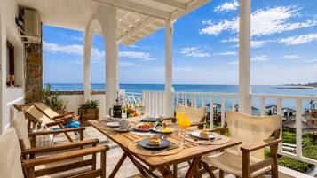 Mesa de madera dispuesta con platos, vasos y una jofaina, con vistas a la costa.