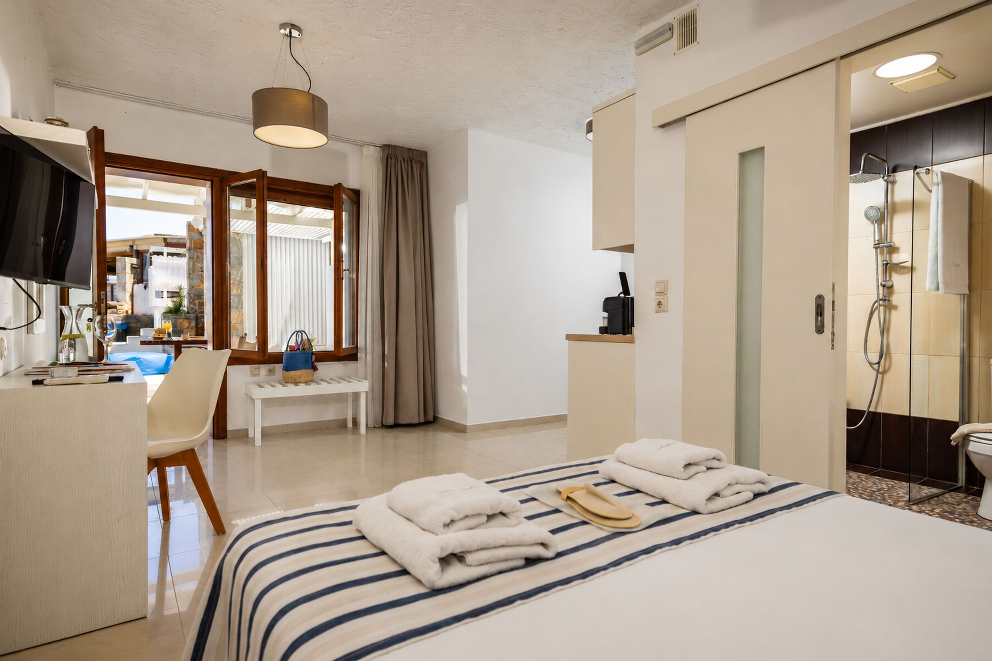 A hotel room with a bed, a desk, a chair, a television, and a shower area.
