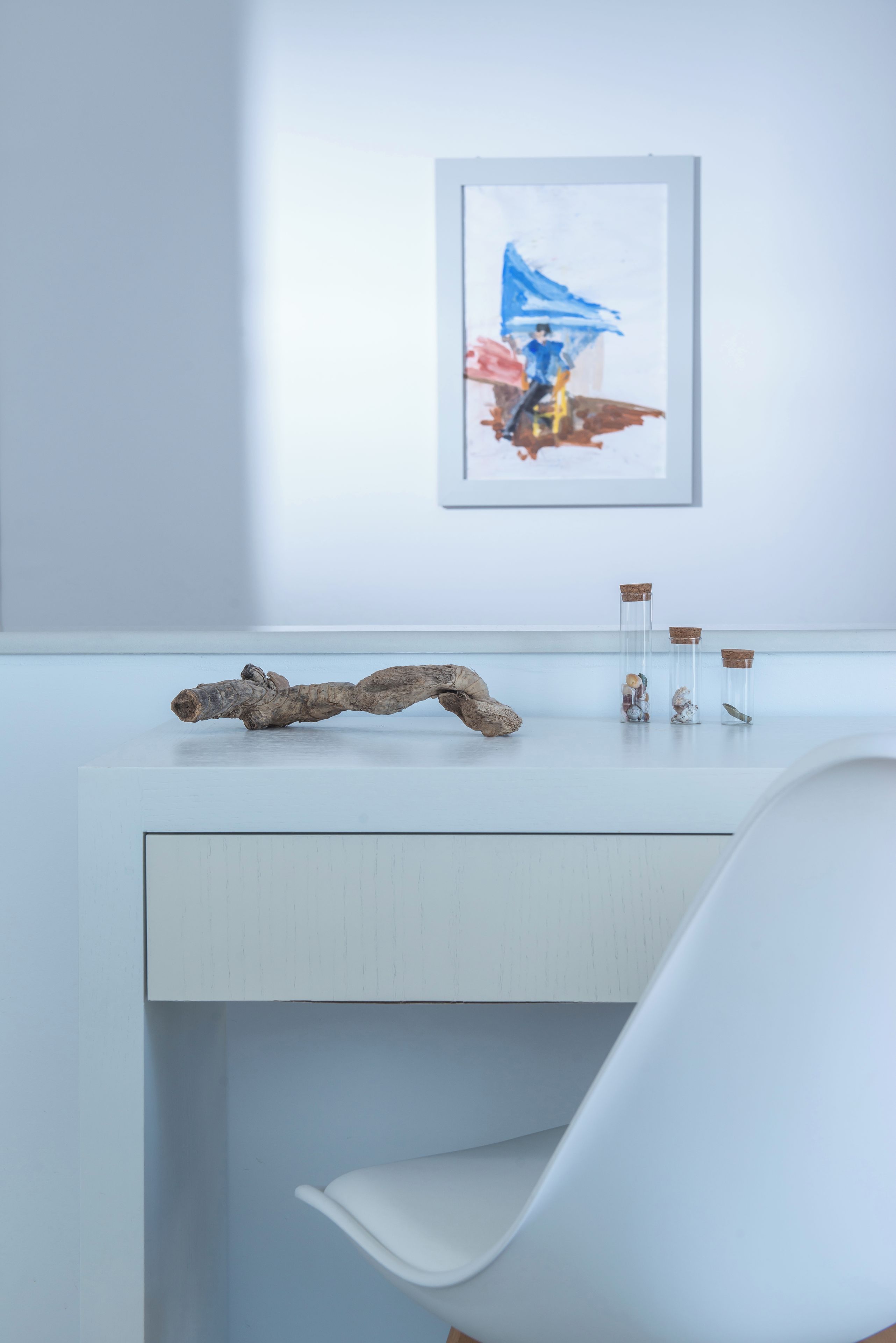 A modern bathroom with a white vanity, a framed artwork on the wall, and a unique wooden piece on the counter.