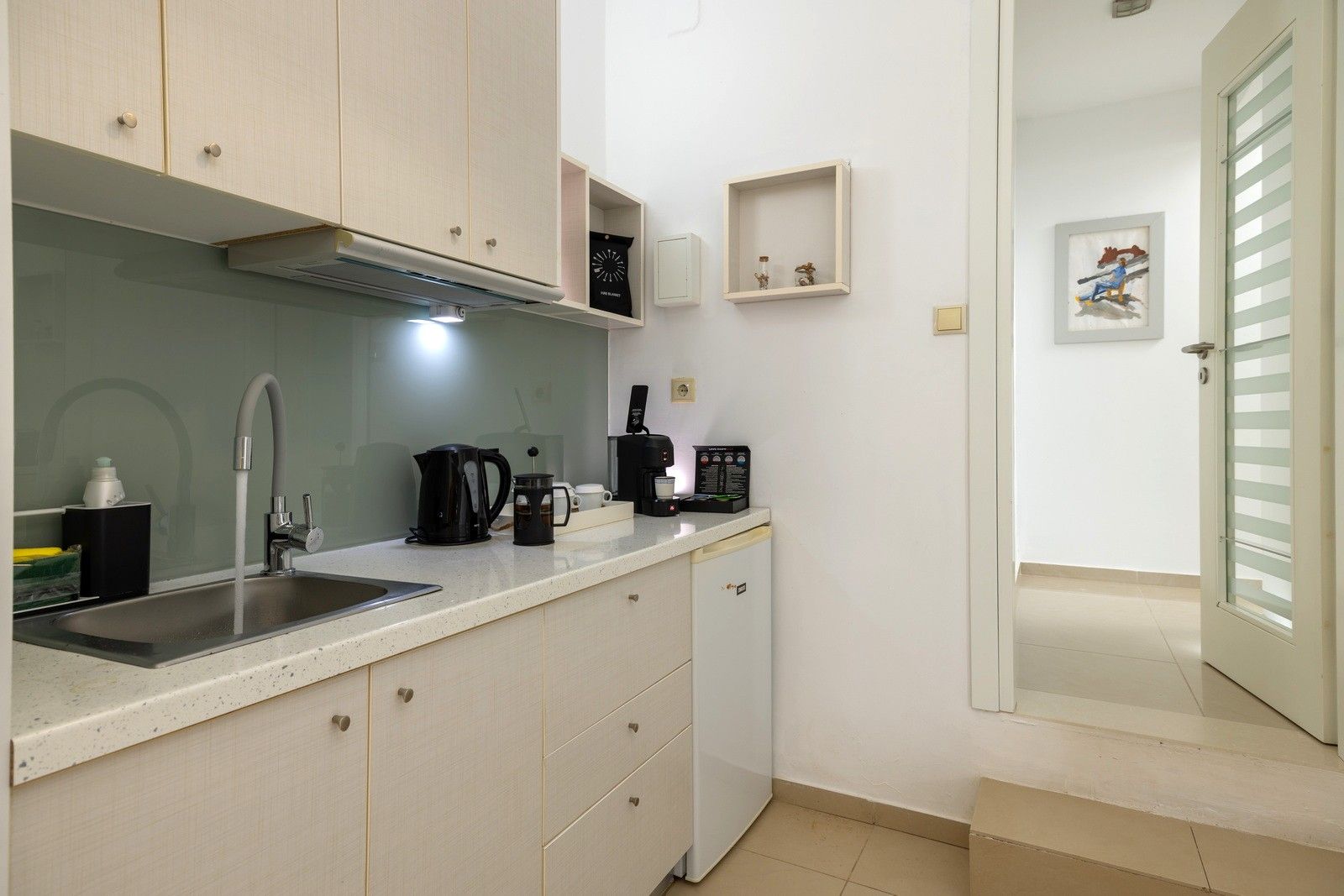 A compact kitchen with a sink, coffee maker, and cabinets.