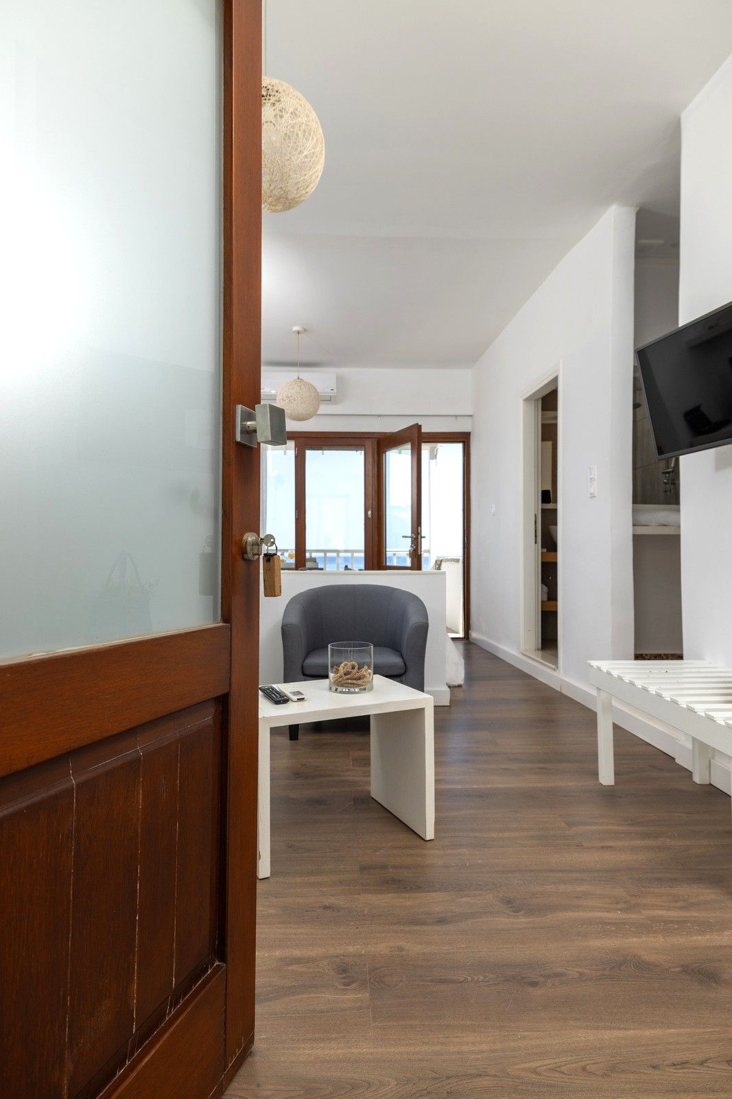 Una sala de estar moderna con piso de madera, un sofá blanco, una mesa de centro de vidrio y un televisor en la pared.