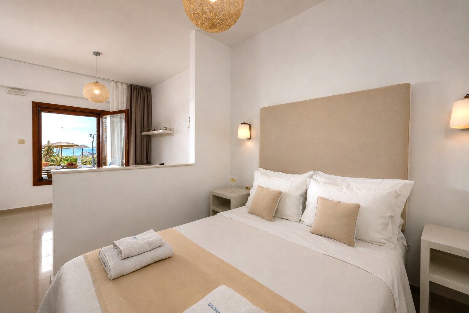 A hotel room with a large bed, a bedside table, a nightstand, a window with curtains, and a view of the outdoors.