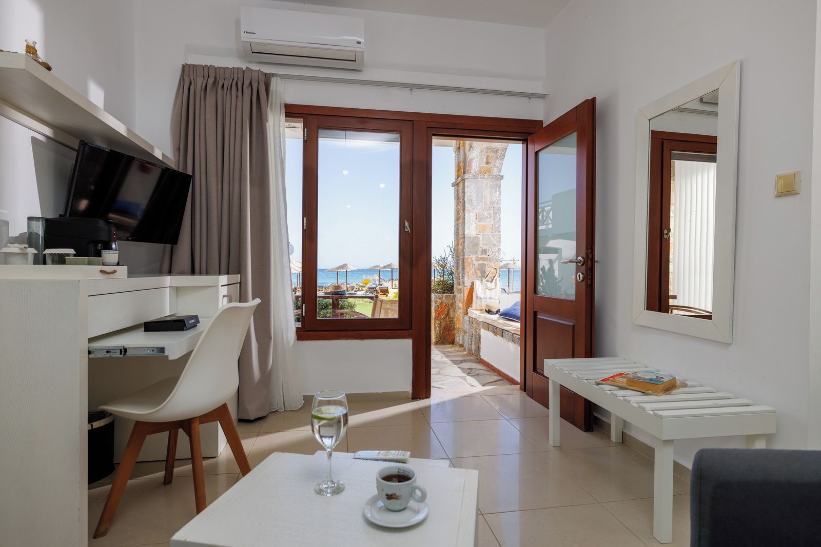 A hotel room with a desk, chair, dining table, and a balcony with a view of the sea.