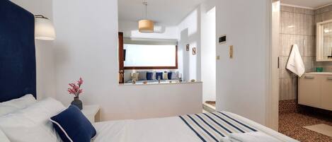 A hotel room with a large bed, a bedside table, a mirror, and a view of the bathroom.