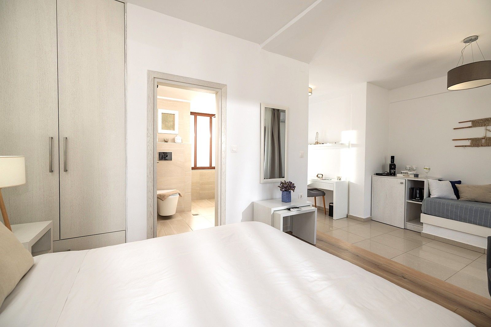A modern hotel room with a large bed, a desk, a sofa, and a wardrobe.