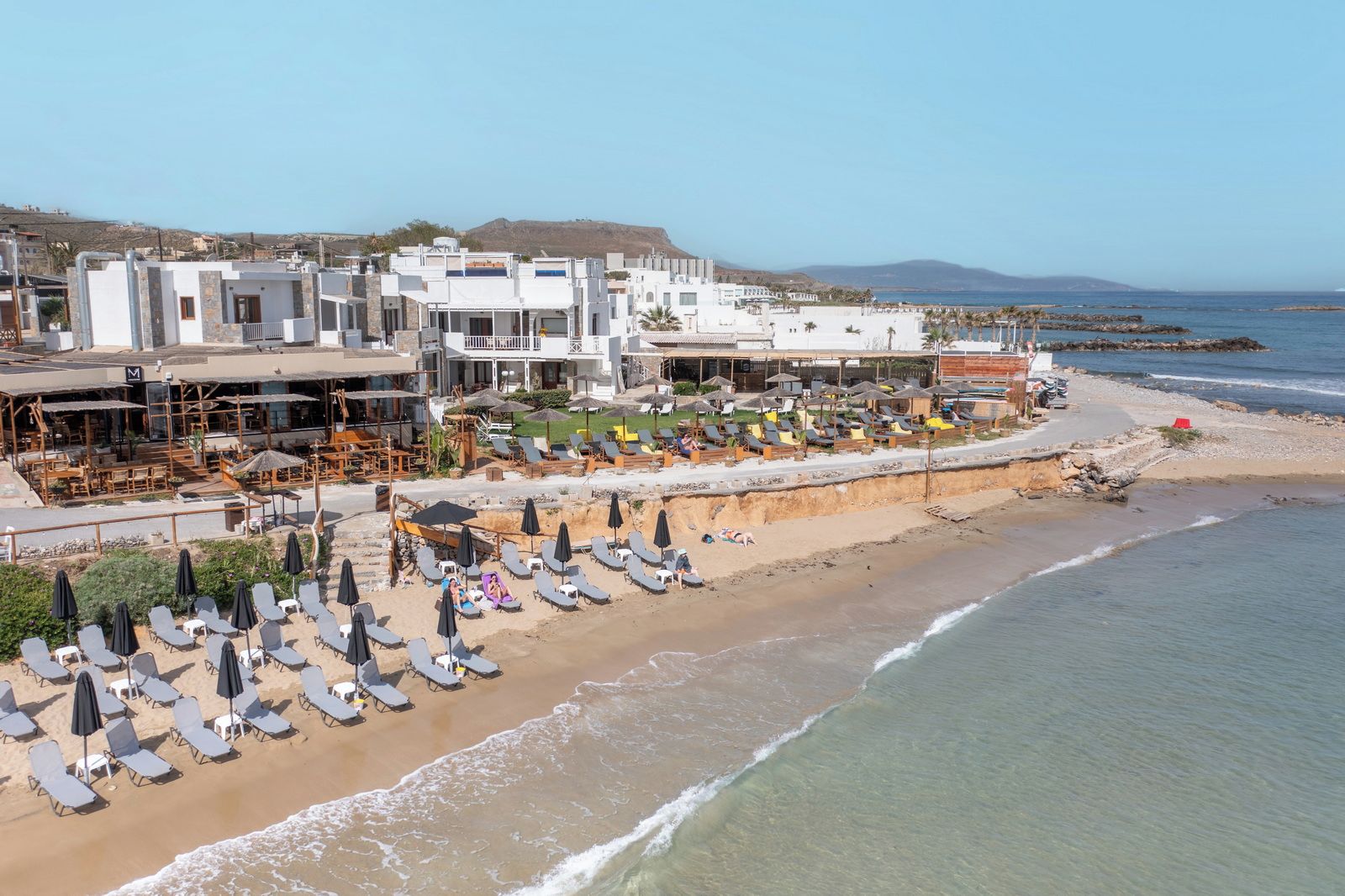 Un hotel frente al mar con varios pisos, sillas de playa y sombrillas.