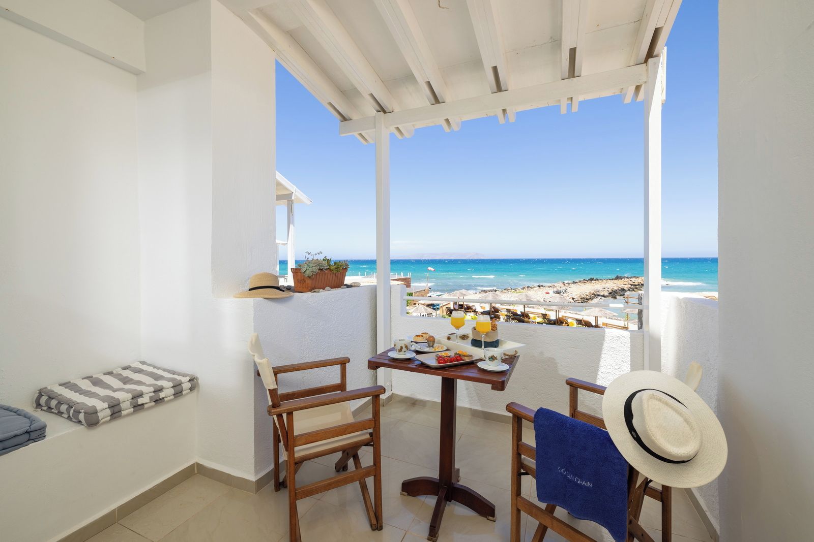 A balcony with a view of the beach, a table with breakfast items, and a chair.