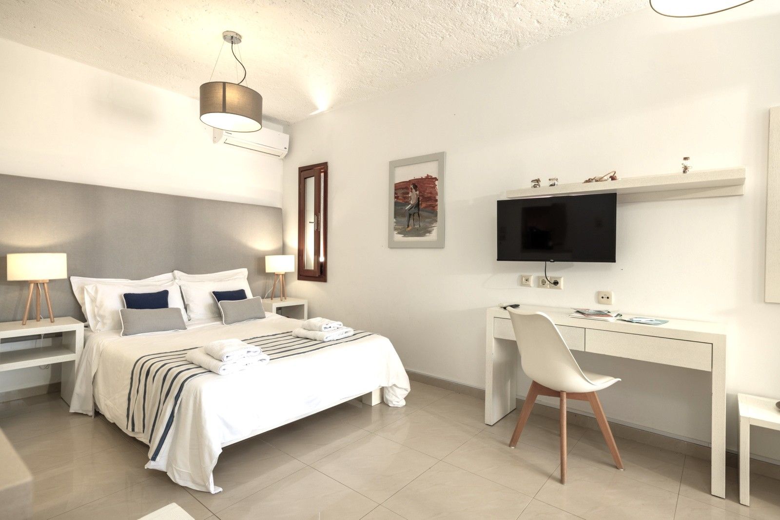 Een moderne hotelkamer met een bed, nachtkastjes, een bureau, een stoel, een televisie en kunstwerken aan de muur.
