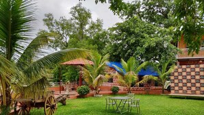 A lush garden with a table and chairs, a wooden cart, and a building with a red roof. - River Retreat Kolad (Kolad)