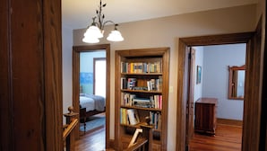 Un escalier en bois mène à une chambre à coucher où se trouvent un lit et une bibliothèque remplie de livres.