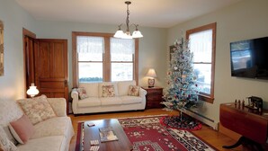 Un salon avec un canapé blanc, une table basse en bois, un sapin de Noël et un téléviseur fixé au mur.