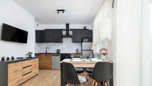 A modern kitchen with a flat-screen TV, dark cabinets, a marble backsplash, and a dining area with a wooden table and black chairs. - Elegant Apartment | Garden, Desk, Parking (Gliwice)