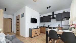 A modern kitchen with dark cabinetry, a built-in oven, and a dining area with a wooden table and black chairs. - Elegant Apartment | Garden, Desk, Parking (Gliwice)
