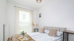 A modern bedroom with a large bed, bedside tables, a window with curtains, and a small table with a tray. - Elegant Apartment | Garden, Desk, Parking (Gliwice)