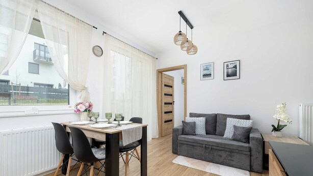 A modern living room with a dining area, a grey sofa, and a wooden floor. - Elegant Apartment | Garden, Desk, Parking (Gliwice)