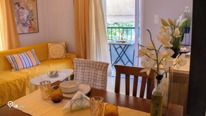 En hyggelig stue med en gul sofa, et spisebord med en vase blomster, og en balkon med bord og stole.