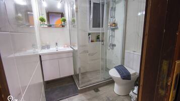 Un baño moderno con ducha de vidrio, lavamanos blanco y un inodoro.