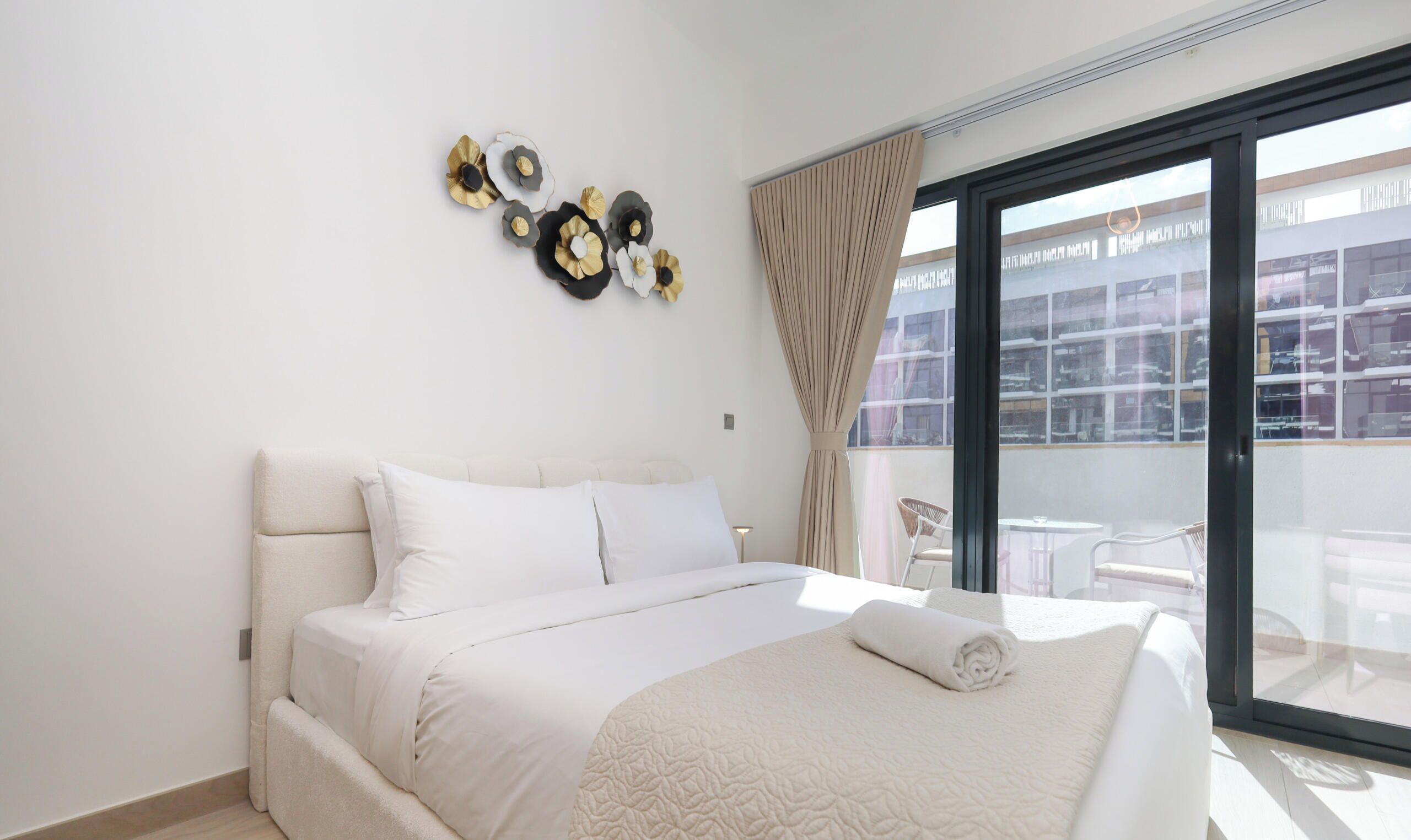 A modern hotel room with a large bed, a balcony with a view of the city, and decorative wall art.