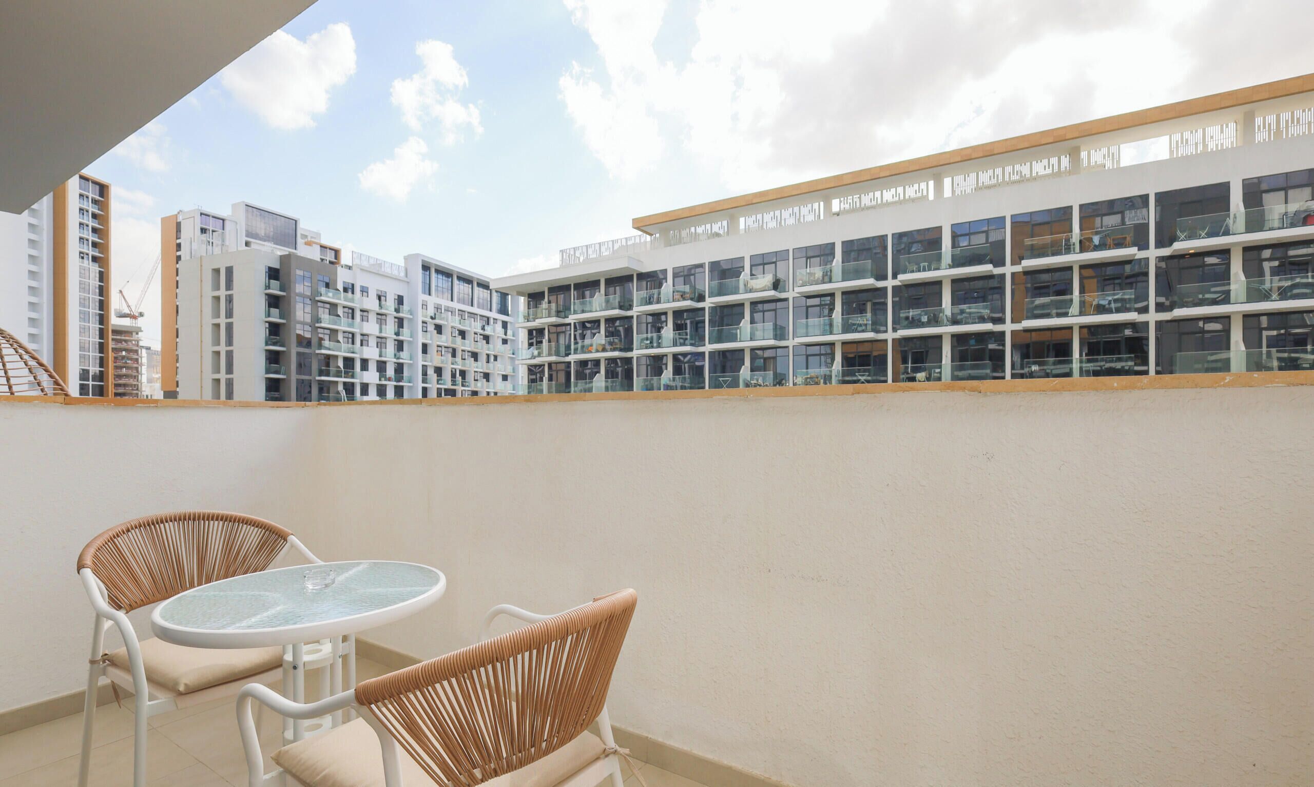 Un balcón con sillas de mimbre y una mesa de vidrio, con vistas a un edificio moderno con varios balcones.