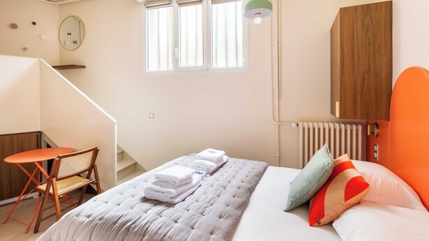 A bedroom with a bed, a chair, a small table, a window, a radiator, and a wooden cabinet. - Port-Royal Residence - Charming Studio - 2P (Paris)