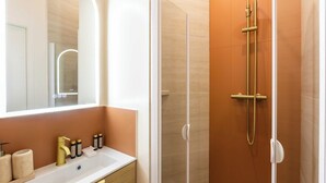 A modern bathroom with a glass-enclosed shower, a white sink with gold fixtures, and a large mirror. - Port-Royal Residence - Charming Studio - 2P (Paris)