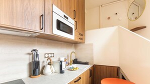 A compact kitchen with wooden cabinets, a built-in oven, a sink, and a small orange table. - Port-Royal Residence - Charming Studio - 2P (Paris)