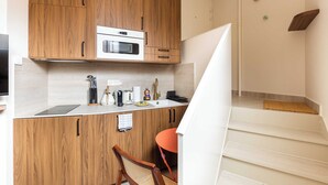 A compact kitchen with wooden cabinets, a built-in oven, and a small dining area with a chair and table. - Port-Royal Residence - Charming Studio - 2P (Paris)