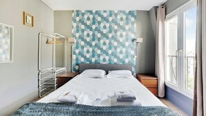 A neatly made bed with towels, a bedside table, a hanging rack, and a patterned wall. - Studio Cosy - 2P - Canal Saint Martin (Paris)