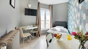 A hotel room with a bed, a dining table with chairs, a small kitchen area, and a window with curtains. - Charming studio - 1P- Canal Saint-Martin (Paris)