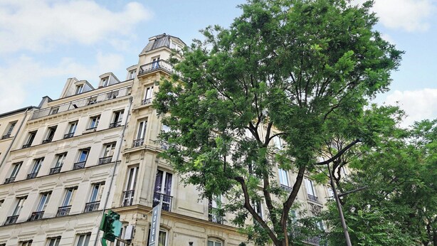 A multi-story hotel with a classic architectural style, featuring balconies and a prominent tree in front. - Charming studio - 1P- Canal Saint-Martin (Paris)