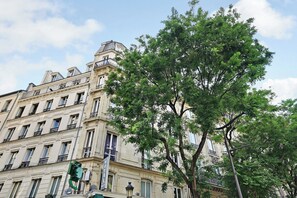 A multi-story hotel with a classic architectural style, featuring balconies and a prominent tree in front. - Charming studio - 1P- Canal Saint-Martin (Paris)