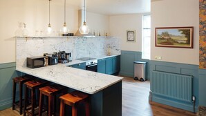 A modern kitchen with a marble countertop, wooden stools, and pendant lighting.