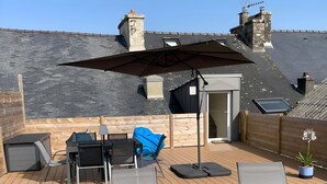 Een houten terras met buitenmeubilair, een parasol en een bloempot.