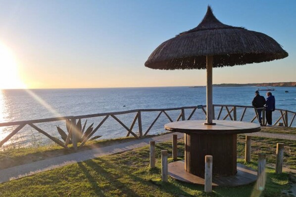 A wooden gazebo with a thatched roof overlooking a body of water, a wooden fence, and a couple of people standing by the railing. - Apartment in heart of Conil (Conil de la Frontera)