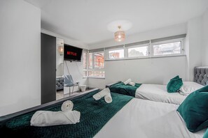 Une chambre d’hôtel avec deux lits, un téléviseur fixé au mur et une fenêtre donnant sur des immeubles.