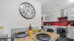 Eine moderne Küche mit einer großen Wanduhr, weißen Schränken und einer roten Spritzschutzwand.