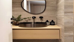 Un baño moderno con un lavabo redondo, un espejo, una planta y dos botellas en la encimera.