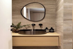 A modern bathroom with a round sink, a mirror, a plant, and two bottles on the countertop. - Cosy and modern studio- Jardin de Luxembourg (Paris)